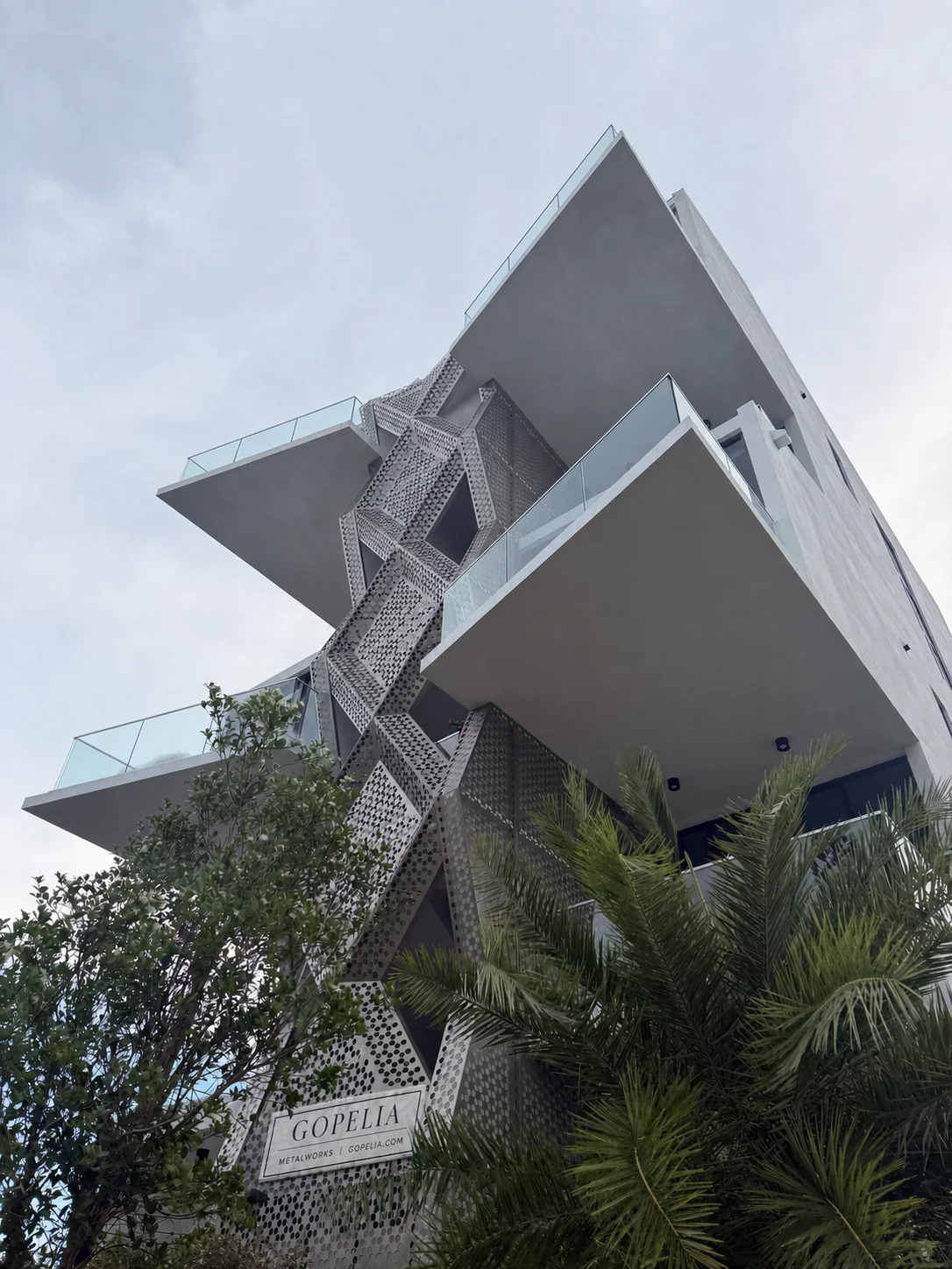 Perforated aluminum diamond stair screen framed by palm - 756 84 St Residences, Miami Beach FL