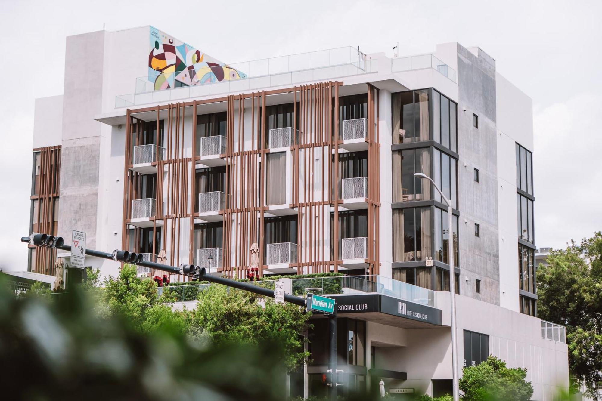 Corner angle of Upsun Hotel showing vertical brown metal facade louvers, perforated metal balcony railings, and rooftop mural - Miami Beach FL