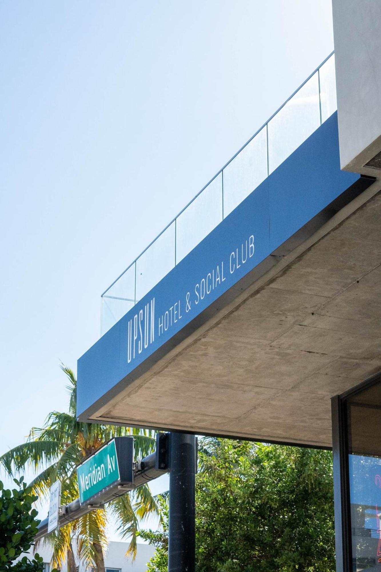 Close-up of UPSUN Hotel & Social Club illuminated signage band with glass railing system above - Miami Beach FL