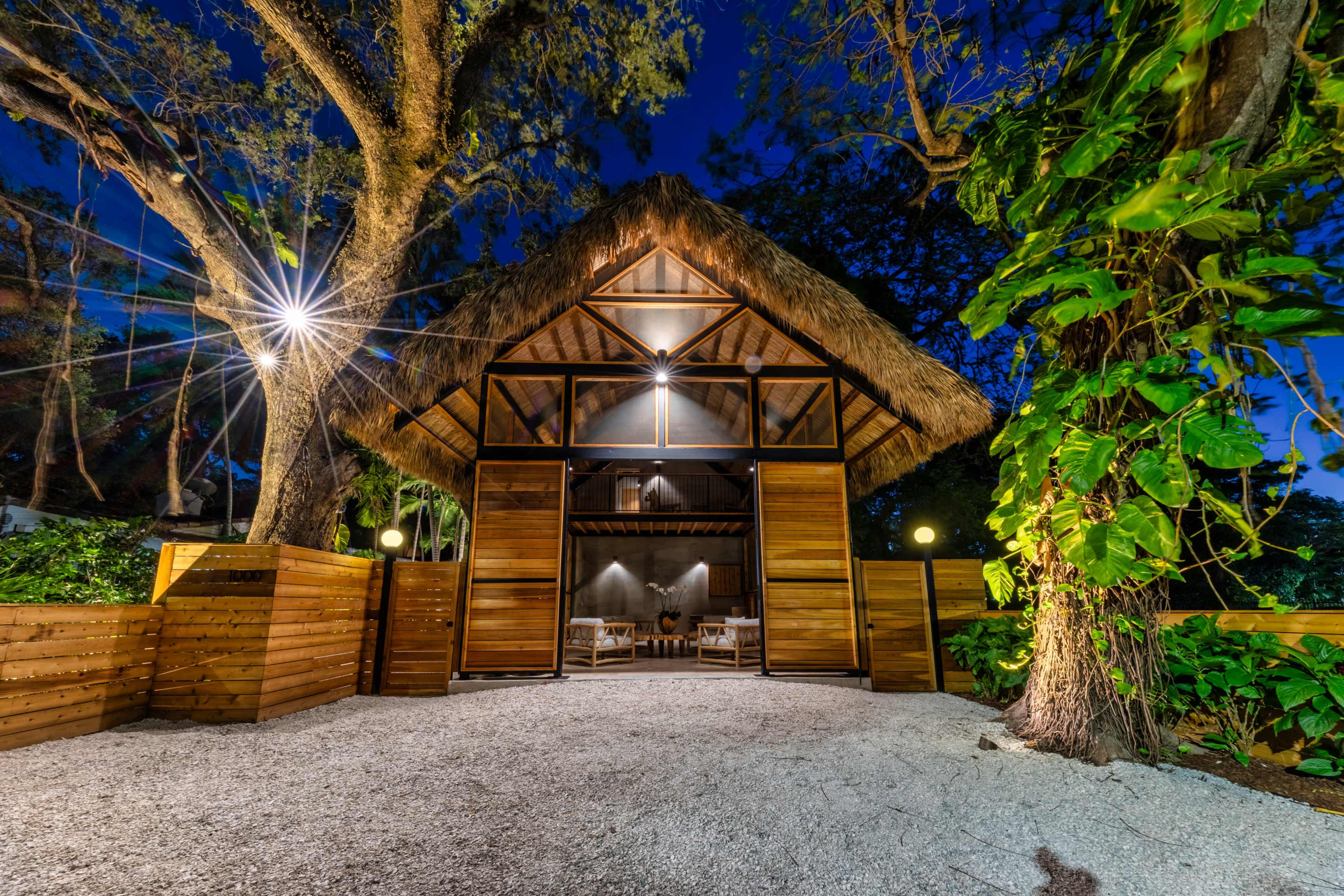 Thatched roof carport gate illuminated at night - Jungle Book Residence, Miami FL