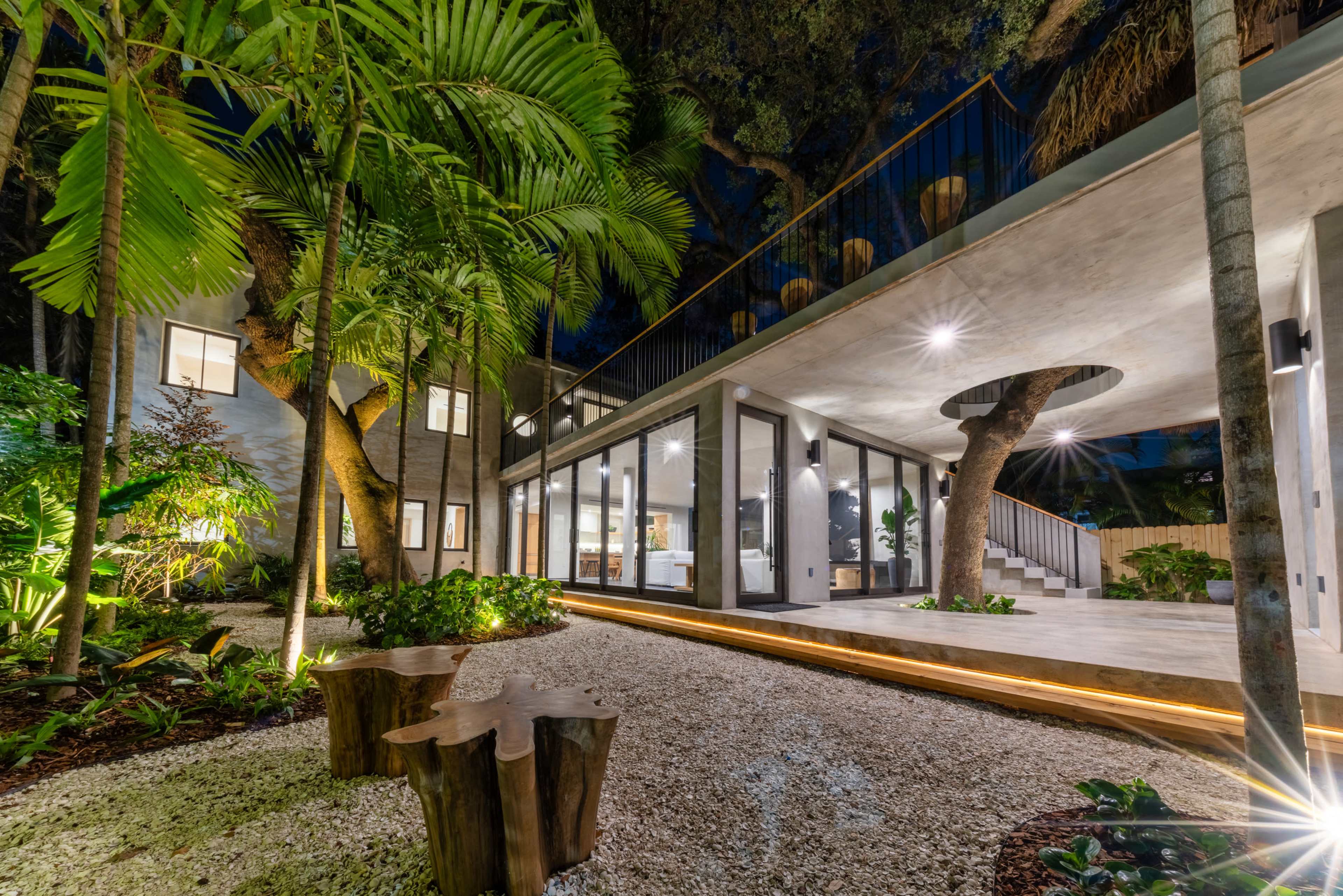 Rear exterior with steel railings and tree surround at night - Jungle Book Residence, Miami FL