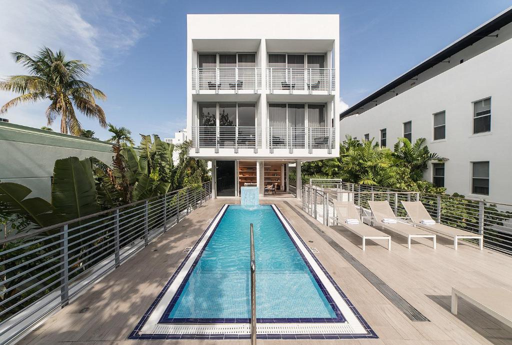 Modern pool deck at The Meridian Hotel featuring a long lap pool, metal railings, deck chairs, and surrounding greenery.