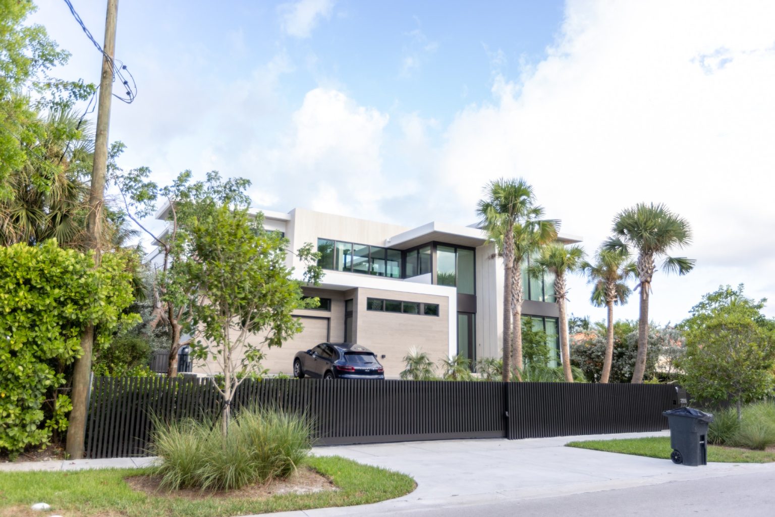 Angled street view of North Bay Village residence in Miami with black aluminum slat fence and driveway