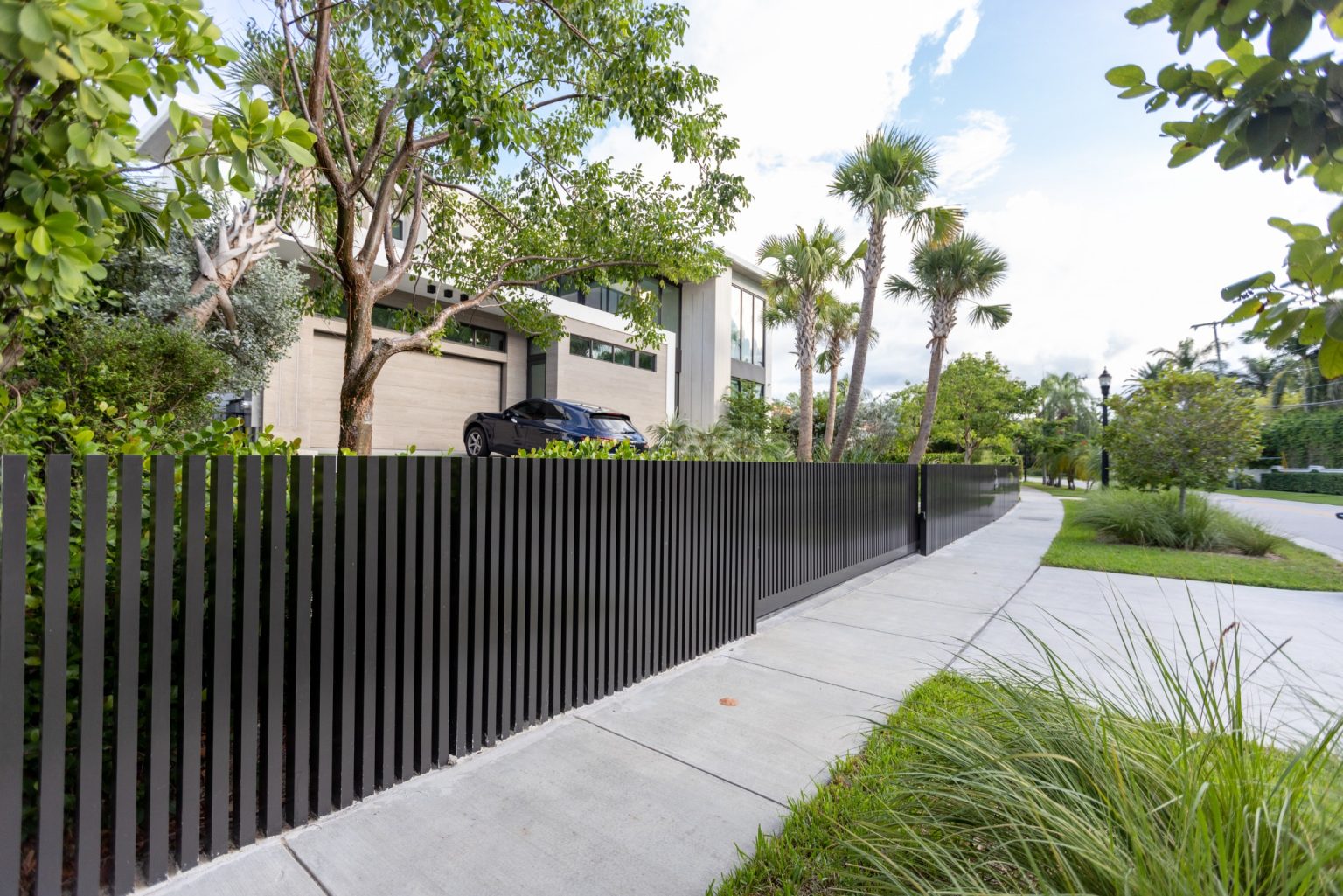 Street view of North Bay Village residence in Miami with black aluminum slat fence and tropical landscaping