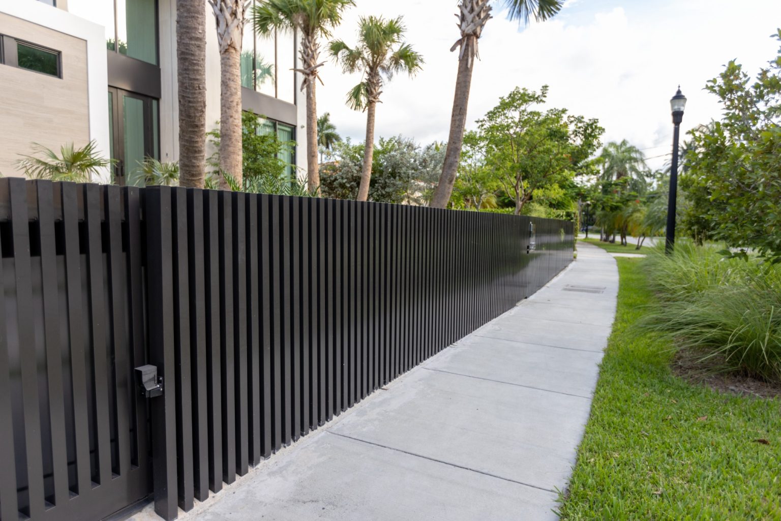 Long sidewalk view of black aluminum slat fence bordering North Bay Village residence in Miami