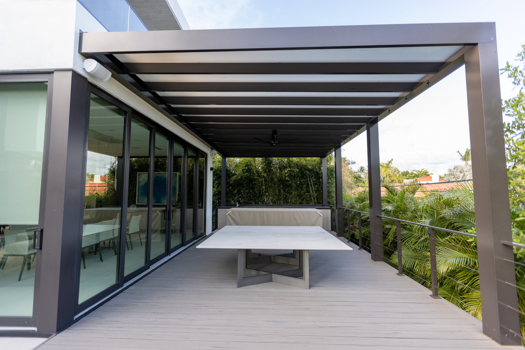 Covered terrace with pergola and dining table adjacent to sliding glass doors at North Bay Village residence in Miami